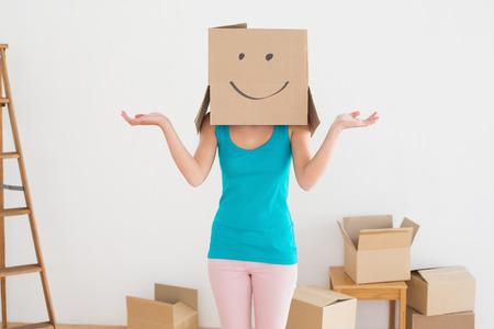 Casual young woman in blue tank top with smiley cardboard box over face in a new houseの写真素材