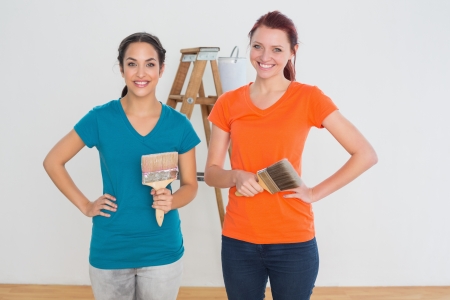 Portrait of two female friends with paint brushes and ladder in a new houseの写真素材