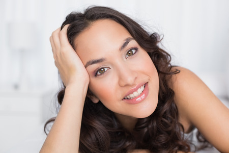 Close-up portrait of a smiling pretty brunette lying in bedの写真素材