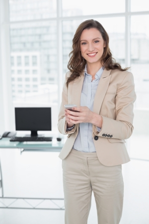 Portrait of a smiling elegant businesswoman text messaging in a bright officeの写真素材