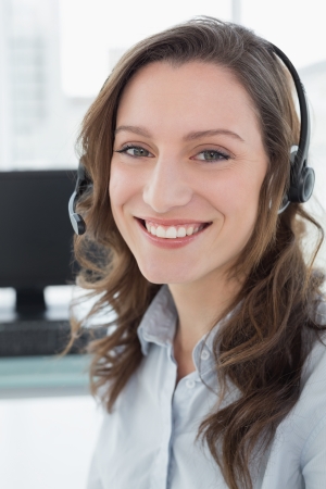 Portrait of businesswoman wearing headset in front of computer in a bright officeの写真素材