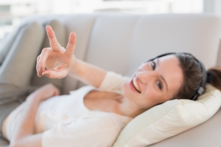 Portrait of a cheerful casual young woman enjoying music on sofa in a bright houseの写真素材