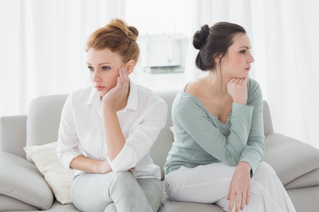 Unhappy young female friends not talking after argument at home on the couchの写真素材