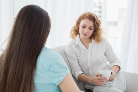 Two young female friends sitting on sofa in the living room at homeの写真素材