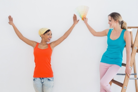 Two happy young female friends with ladder choosing color for painting a room in new houseの写真素材