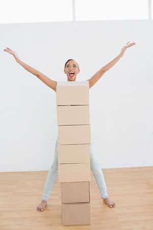 Cheerful young woman shouting with stack of boxes in a new houseの写真素材