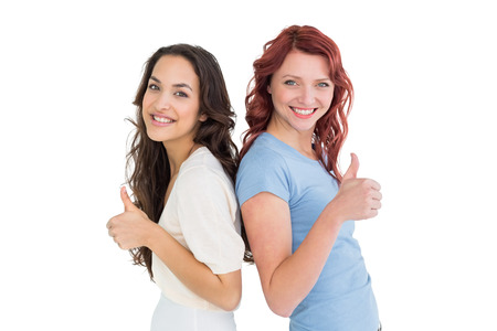 Portrait of two young female friends gesturing thumbs up over white backgroundの写真素材