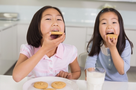 Portrait of two smiling young girls enjoying cookies and milk in the kitchenの写真素材