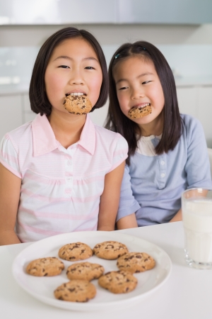 Portrait of two smiling young girls enjoying cookies and milk in the kitchenの写真素材