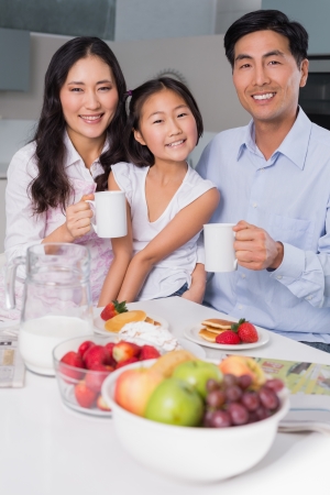 Portrait of a happy young girl enjoying breakfast with parents at table in the houseの写真素材