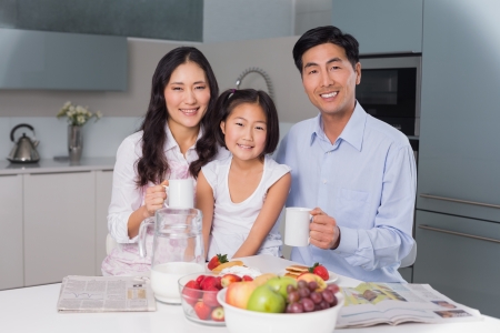 Portrait of a happy young girl enjoying breakfast with parents at table in the houseの写真素材