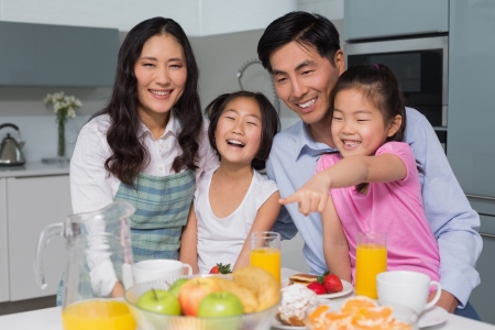 Portrait of a cheerful family of four enjoying healthy breakfast in the kitchen at homeの写真素材