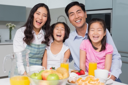 Portrait of a cheerful family of four enjoying healthy breakfast in the kitchen at homeの写真素材