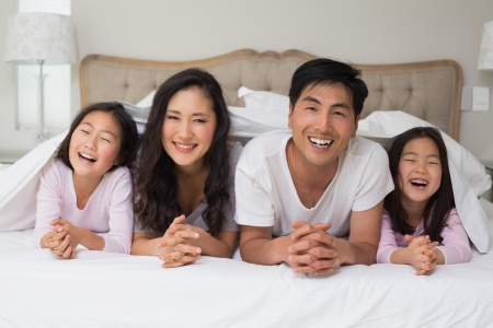 Portrait of a cheerful family of four lying in bed at homeの写真素材
