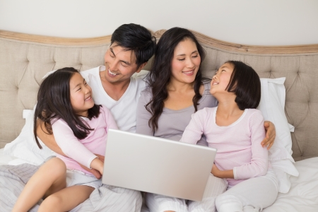 Happy relaxed family of four using laptop in bed at homeの写真素材
