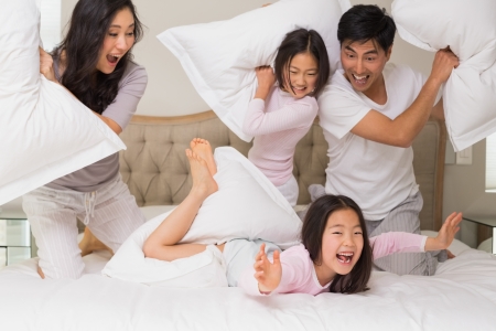 Cheerful kids and parents  having pillow fight on bed at homeの写真素材