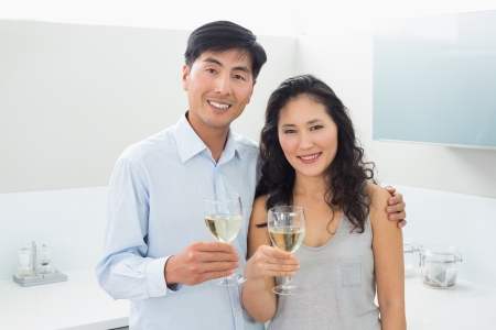Portrait of a loving young couple with wine glasses in the kitchen at homeの写真素材