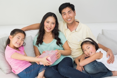 Family presenting happy mother with a gift box in the living room at homeの写真素材