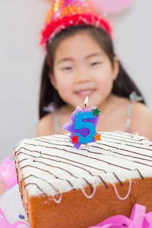 Close-up of a blurred little girl with lit candle on birthday cakeの写真素材