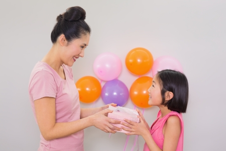 Side view of a woman giving gift box to a little girl at a birthday partyの写真素材