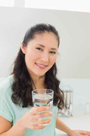 Close-up portrait of a young woman with a glass of water in the kitchen at homeの写真素材
