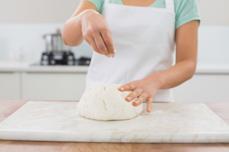 Close-up mid section of a woman kneading dough in the kitchen at homeの写真素材