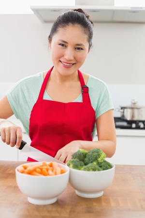 Portrait of a smiling young woman chopping vegetables in the kitchen at homeの写真素材