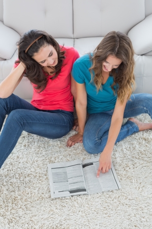 High angle view of two young female friends reading a book in the living room at homeの写真素材