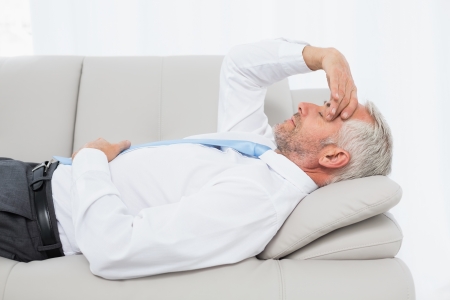 Side view of a tired mature businessman resting on sofa in the living room at homeの写真素材