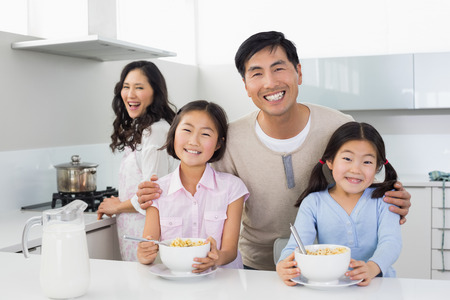 Portrait of a smiling couple with happy two daughters having breakfast in the kitchen at homeの写真素材