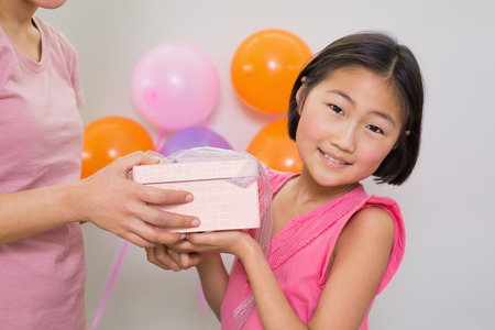 Close-up side view of a woman giving gift box to a little girl at a birthday partyの写真素材