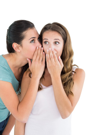 Two young female friends gossiping over white backgroundの写真素材