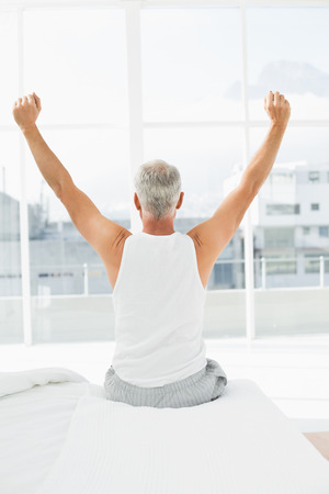 Rear view of a mature man waking up in bed and stretching his armsの写真素材