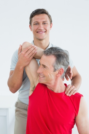 Portrait of a male physiotherapist stretching a mature mans arm in the hospitalの写真素材