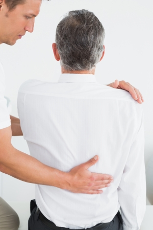 Rear view of a male chiropractor examining mature man at officeの写真素材