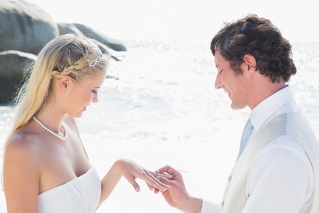 Man placing ring on happy brides finger at the beachの写真素材