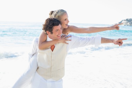 Newlyweds pointing to something and smiling at the beachの写真素材