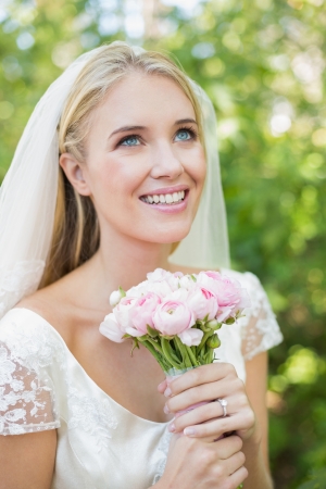 Smiling bride holding her bouquet wearing a veil looking up in the countrysideの写真素材
