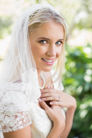 Blonde smiling bride in a veil holding her hands to her chest in the countrysideの写真素材
