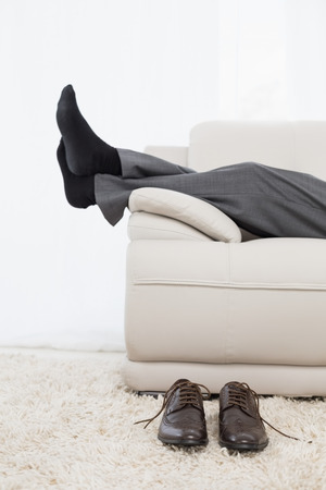 Low section side view of a businessman resting on sofa in the living room at homeの写真素材