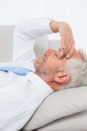 Close-up side view of a tired mature businessman resting on sofa in the living room at homeの写真素材