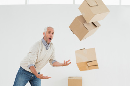 Side view of a mature man with falling boxes against white backgroundの写真素材