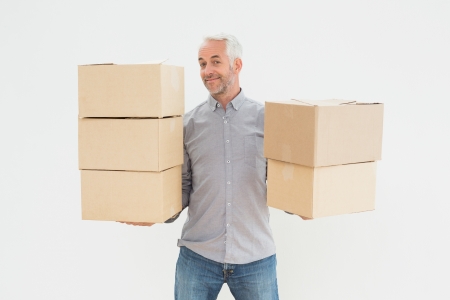 Portrait of a smiling mature man carrying boxes against white backgroundの写真素材