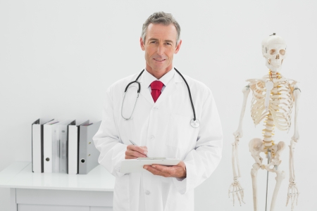 Portrait of a confident male doctor writing a report at the medical officeの写真素材