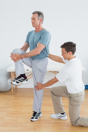 Side view of a male therapist helping man with stretching exercises in the gym at hospitalの写真素材