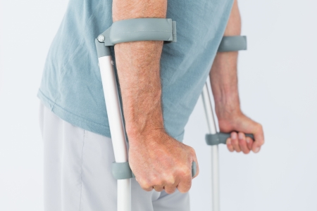 Close-up mid section of a man with crutches standing against white backgroundの写真素材