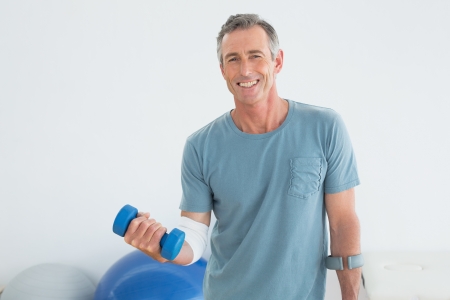 Portrait of a smiling mature man with crutch and dumbbells at the gym hospitalの写真素材