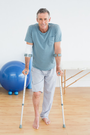 Full length portrait of a smiling mature man with crutches at the gym hospitalの写真素材
