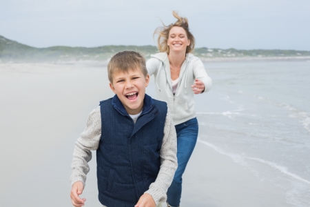 Smiling young woman and cheerful boy running at the beachの写真素材