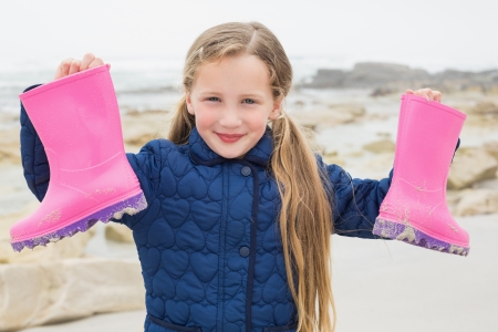 Portrait of a cute smiling young girl holding her wellington boots at the beachの写真素材